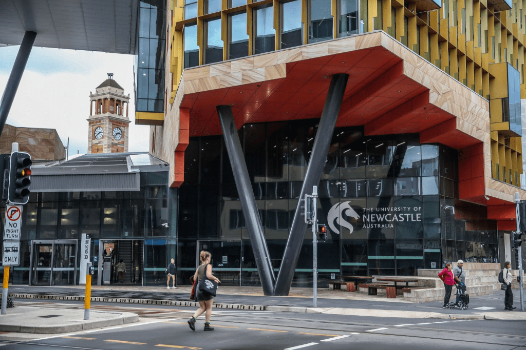 Front entrance of the University of Newcastle, Australia, featuring its modern city campus building, a pedestrian crossing, and surrounding streetscape, representing a study destination for international students and skilled migrants.